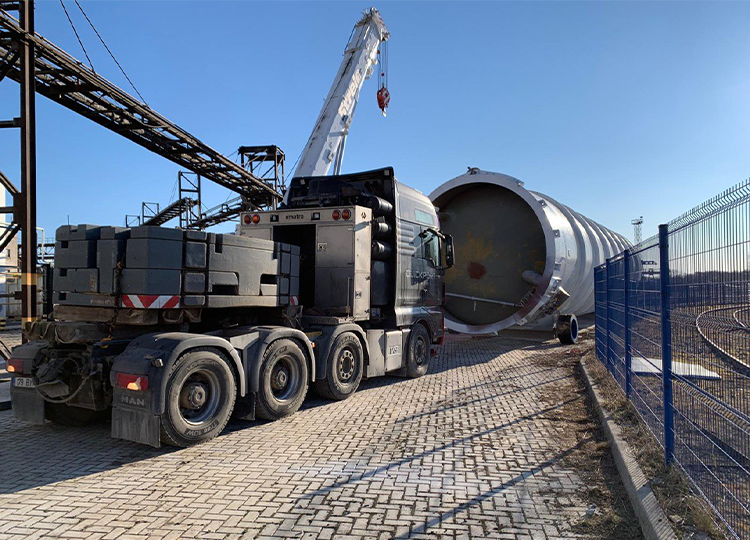 Truck-mounted crane positioning heavy industrial tank section at industrial facility